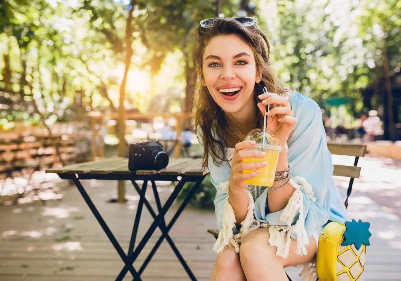 Portret van een jonge, aantrekkelijke, stijlvolle vrouw, zittend in een café, oprecht glimlachend, een sap-smoothie drinkend, gezonde levensstijl, street-bohostijl, modieuze accessoires, lachend, gelukkige emotie, zonnig.